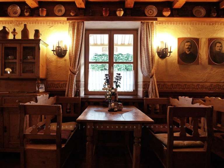 Das Bild zeigt eine gemütliche, traditionelle Gaststube mit Holztischen und -stühlen sowie Wanddekorationen.