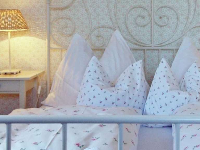 Ein Nachttisch mit einer Lampe steht neben einem Bett mit vielen Kissen und einer Bettdecke mit Blumenmuster.