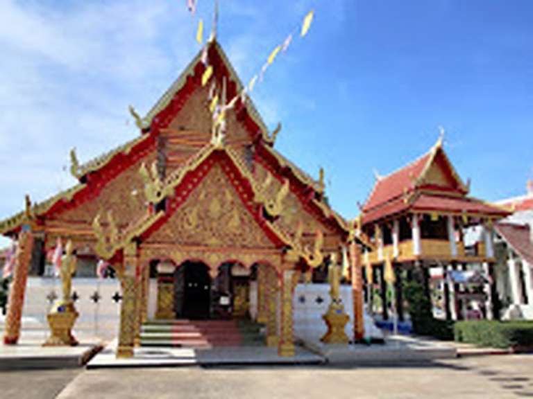Ein buddhistischer Tempel mit goldenen und roten Verzierungen steht unter einem blauen Himmel.