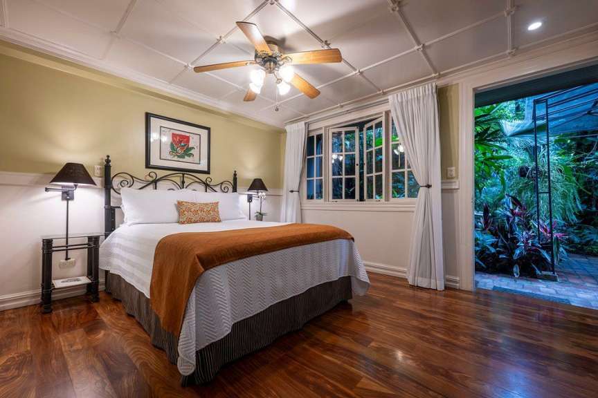 Ein Schlafzimmer mit einem Bett, einem Deckenventilator und einem Blick auf einen üppigen tropischen Garten.