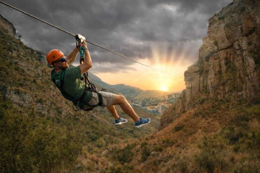 Ein Mann fährt am späten Nachmittag in Südafrika mit der Golden Gate Zipline über eine hügelige Canyon-Landschaft.