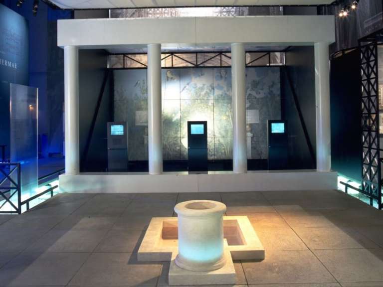Eine museale Installation im Pont du Gard Museum in Frankreich mit klassischen Säulen, Bildschirmen und einem Brunnen.