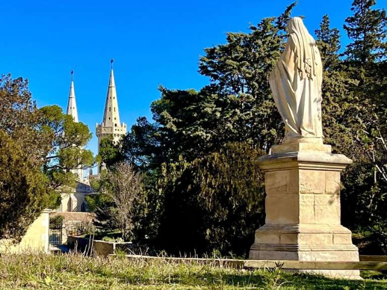 Eine Steinstatue im Vordergrund blickt auf die historischen Türme der Abbaye Saint-Michel de Frigolet in Frankreich.