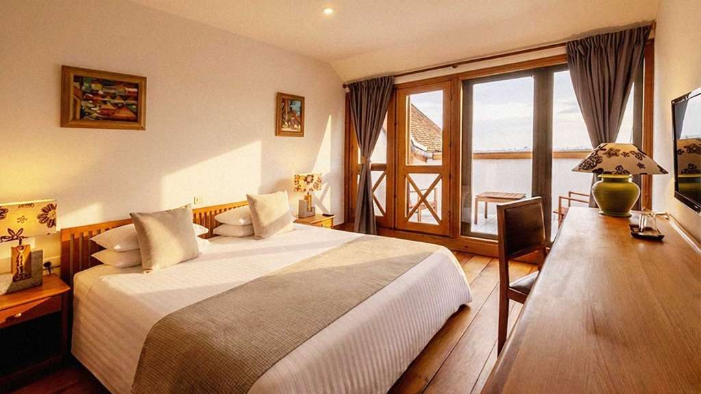 Ein helles Hotelzimmer mit großem Doppelbett, Schreibtisch und Glastüren zur Terrasse am späten Nachmittag in Madagaskar.