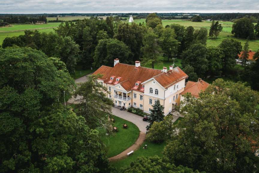 Ein historischer Gutshof im estnischen Nationalpark liegt eingebettet in eine grüne Wald- und Wiesenlandschaft unter bedecktem Himmel.