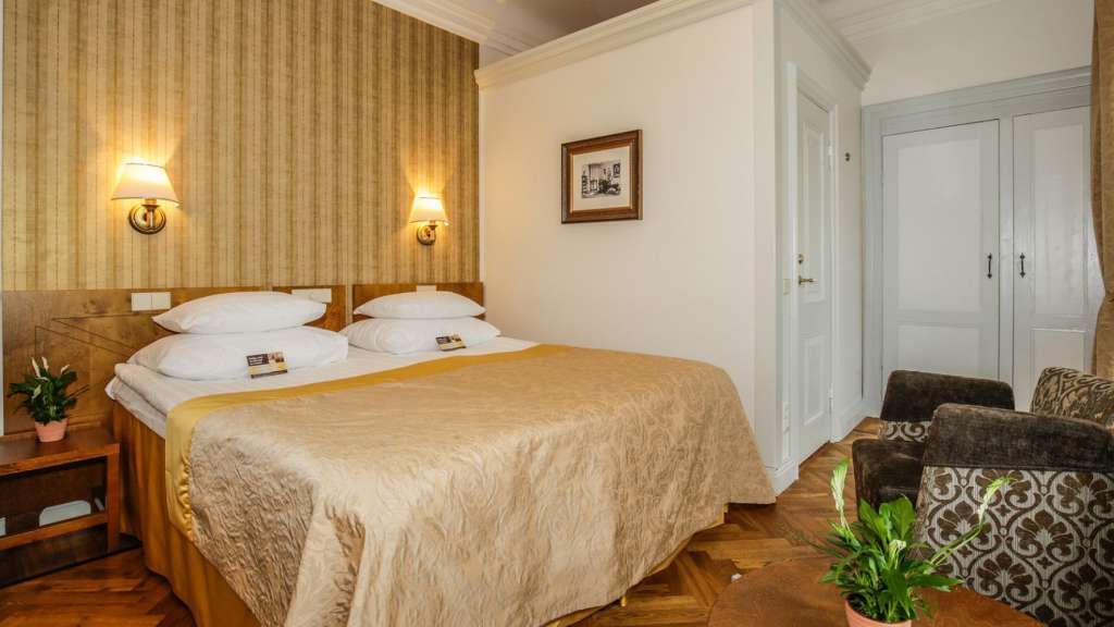 Ein Hotelzimmer in Estland mit einem großen Doppelbett, zwei Sesseln und klassischer Wandverkleidung.