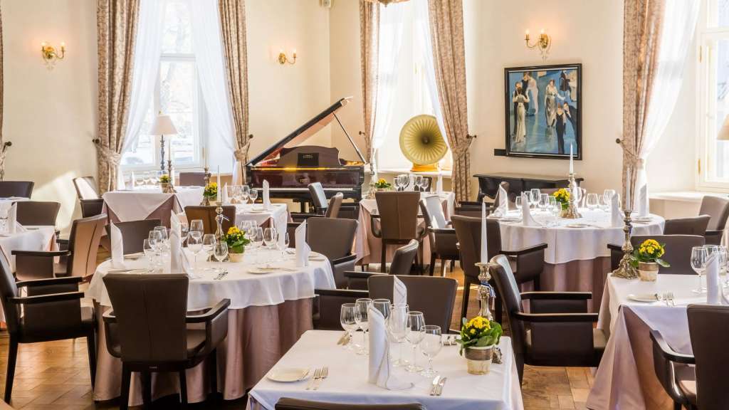 Elegantes Restaurant mit gedeckten Tischen, einem Konzertflügel und großen Fenstern mit Tageslicht.