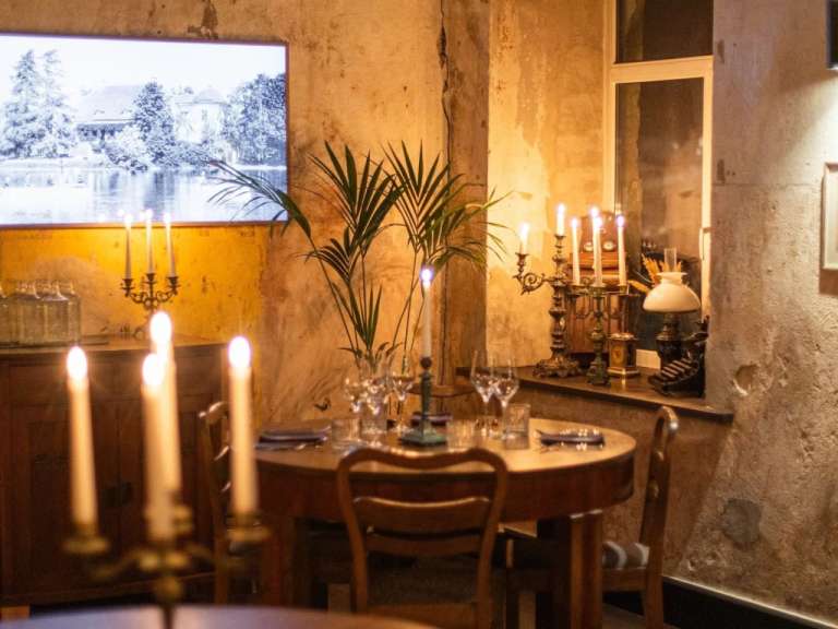 Gemütlich beleuchteter Gastraum eines Restaurants in Estland mit Holztischen, Kerzenständern und einer winterlichen Landschaftsdarstellung an der Wand.