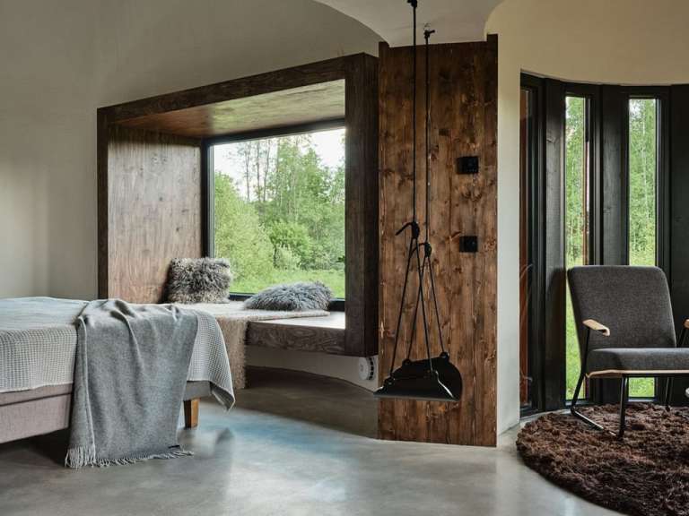 Ein modernes Interieur der Villa Poku in Estland mit Holzakzenten, einem gemütlichen Fensterplatz und Blick ins Grüne.