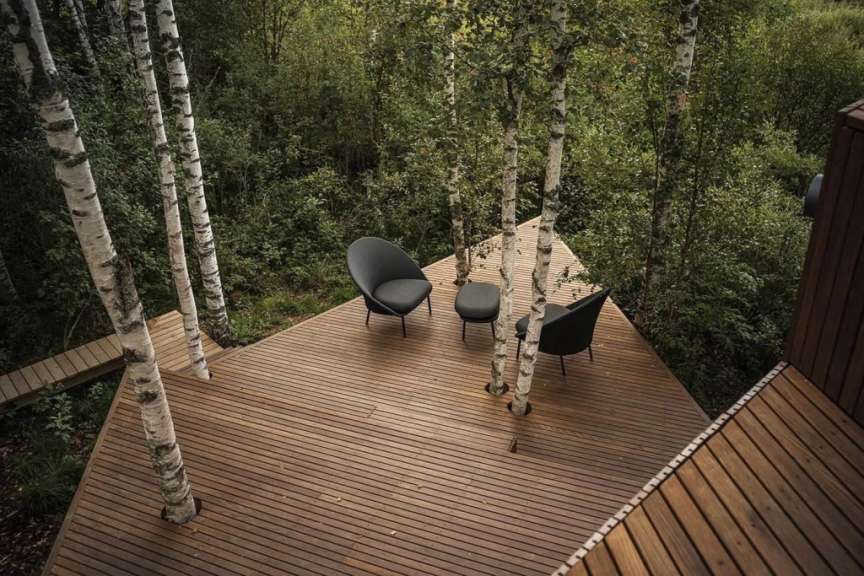 Eine hölzerne Terrasse einer Villa im Wald von Estland ist mit zwei Sesseln und einem kleinen Hocker ausgestattet.