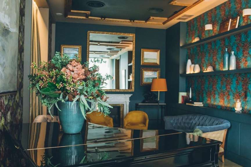 Stilvolles Hotelinterieur mit einem Flügel, floraler Dekoration, gemütlichen Sesseln und blau gemusterten Wänden in Spanien.