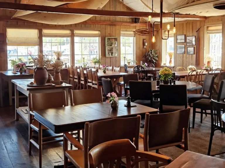 Gemütliches Restaurant in Schweden mit Holztischen und Stühlen vor großen Fenstern, die Tageslicht hereinlassen.
