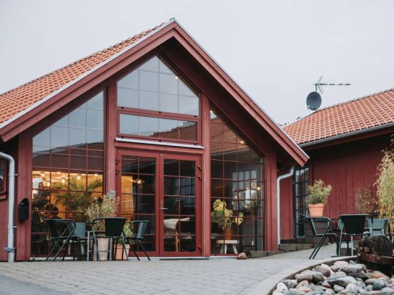 Rotes Holzhaus mit großer Glasfront und Terrasse im Tageslicht.