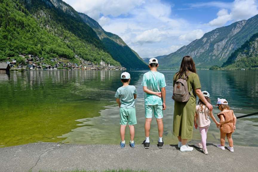 Eine Mutter mit vier Kindern steht am Ufer des Hallstätter Sees in Österreich und blickt auf die umliegende Berglandschaft.
