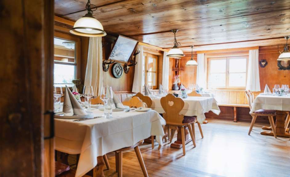 Gemütlicher Gastraum eines traditionellen Restaurants in Österreich mit holzverkleideten Wänden und eingedeckten Holztischen bei Tageslicht.