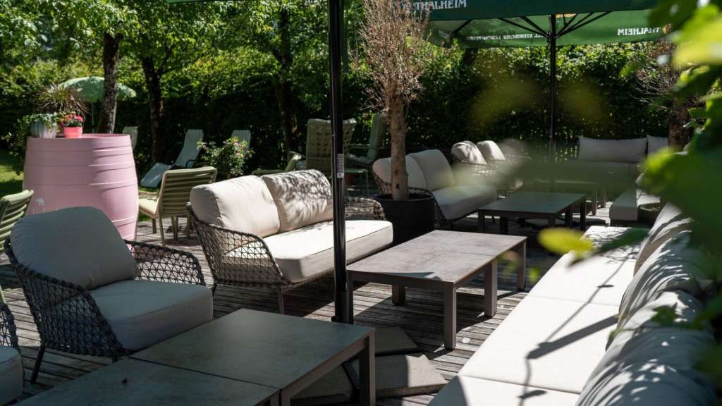 Gemütliche Outdoor-Lounge mit Sofas, Sesseln und Sonnenschirmen auf einer Holzterrasse im Grünen in Österreich.