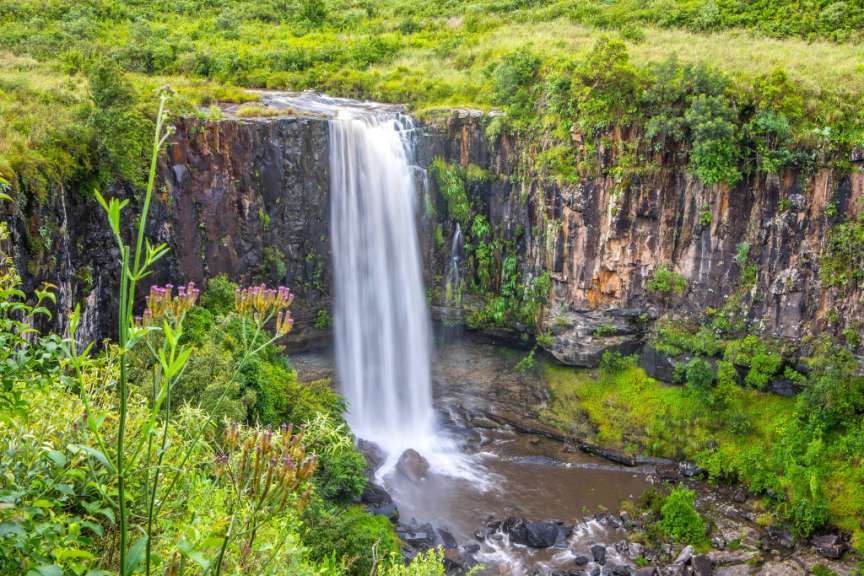 Blick auf den Wasserfall Sterkspruit Falls in einer grünen südafrikanischen Hügellandschaft mit steilen Felswänden.