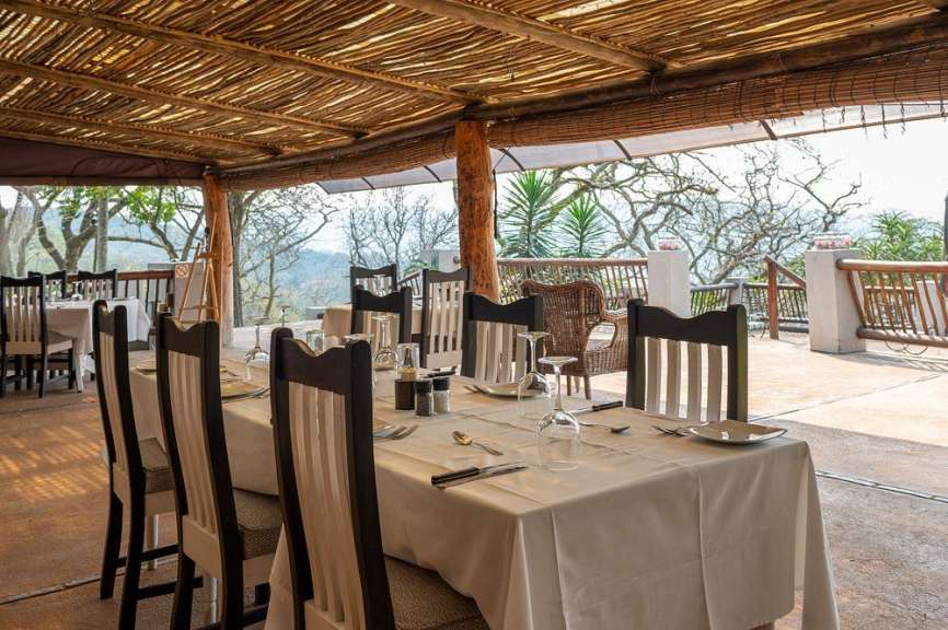 Gedeckter Tisch unter einer Schilfdach-Terrasse mit Blick auf Bäume in Südafrika.