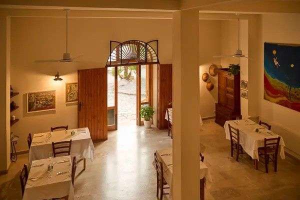 Ein schlichter Speisesaal in Italien mit eingedeckten Tischen, weiß gedeckten Tischen und einer weiten Holztür, die nach draußen führt.