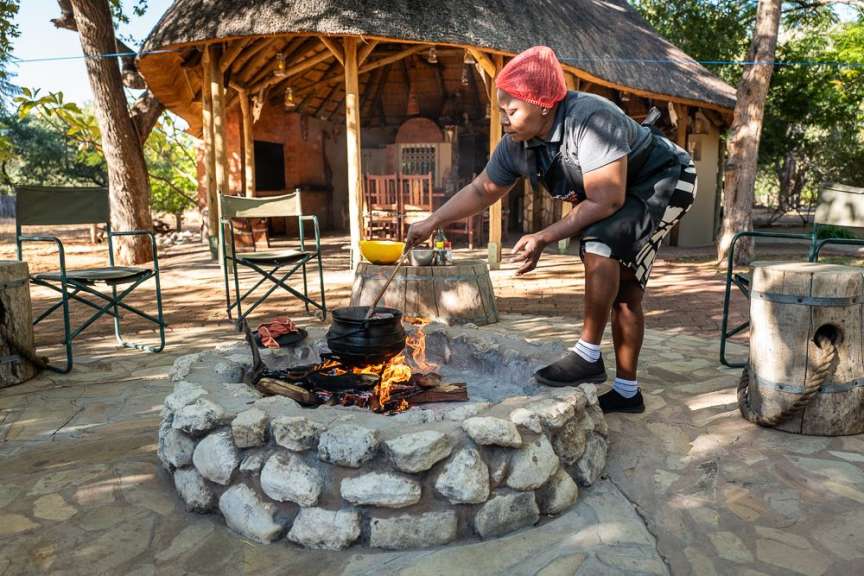 Eine Frau bereitet tagsüber am Grillplatz in Namibia mit einem Topf auf offenem Feuer eine Mahlzeit zu.