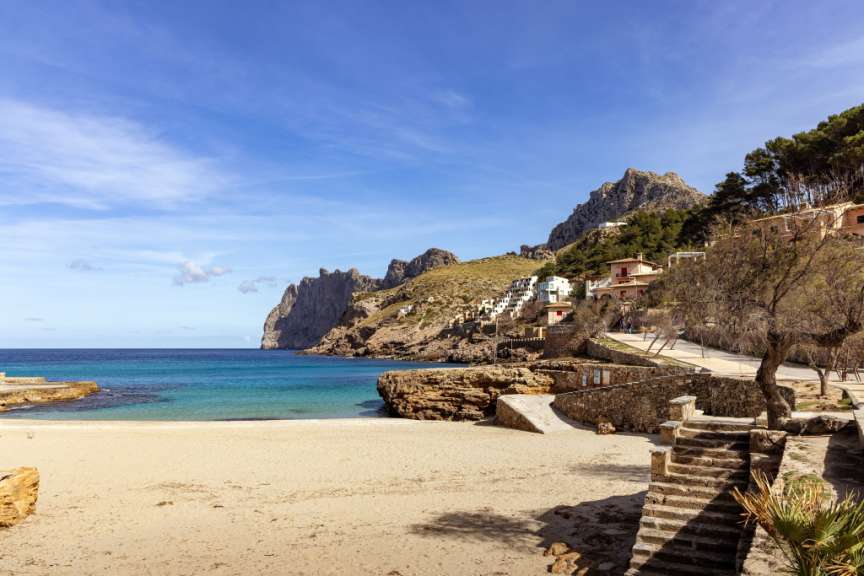 Die Bucht Cala Sant Vicenç auf Mallorca zeigt einen Sandstrand und Häuser am Fuße schroffer Berge.
