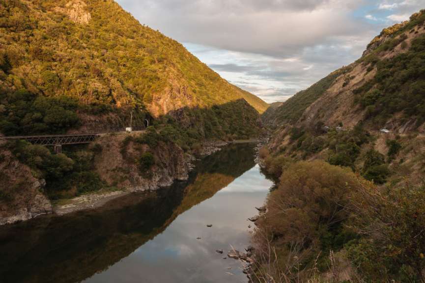 Ein Fluss schlängelt sich durch ein von Bergen gesäumtes Tal, mit einer Brücke und einem Tunnel auf der linken Seite.