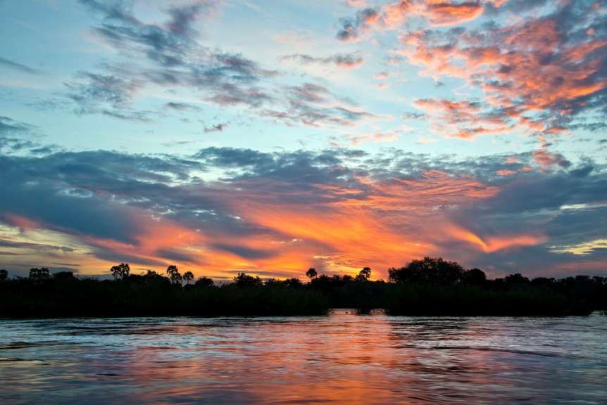 Ein Sonnenuntergang über einem Fluss mit Bäumen im Hintergrund