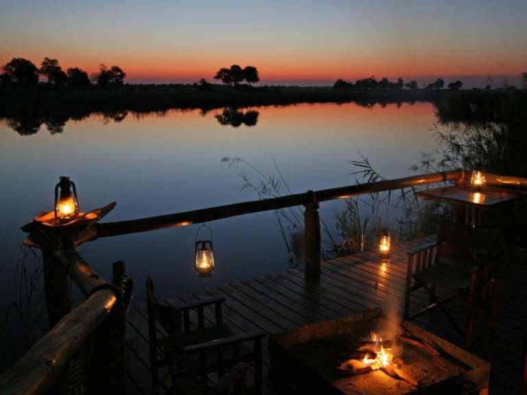 Ein romantischer Ausblick auf einen See bei Sonnenuntergang mit Lagerfeuer und Laternen.