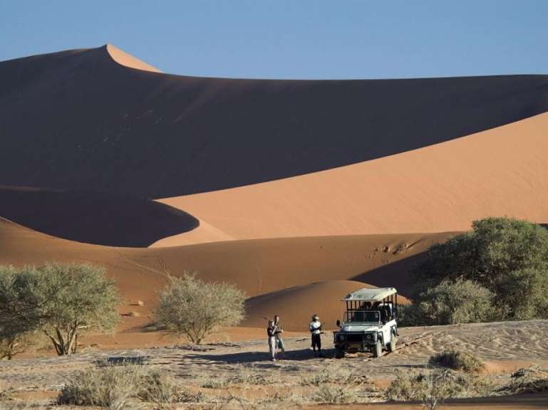 Eine Gruppe von Menschen steht neben einem weißen Jeep in der Wüste