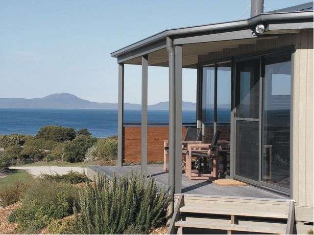 Eine hölzerne Terrasse mit Blick auf das Meer und eine Bergkette im Hintergrund.