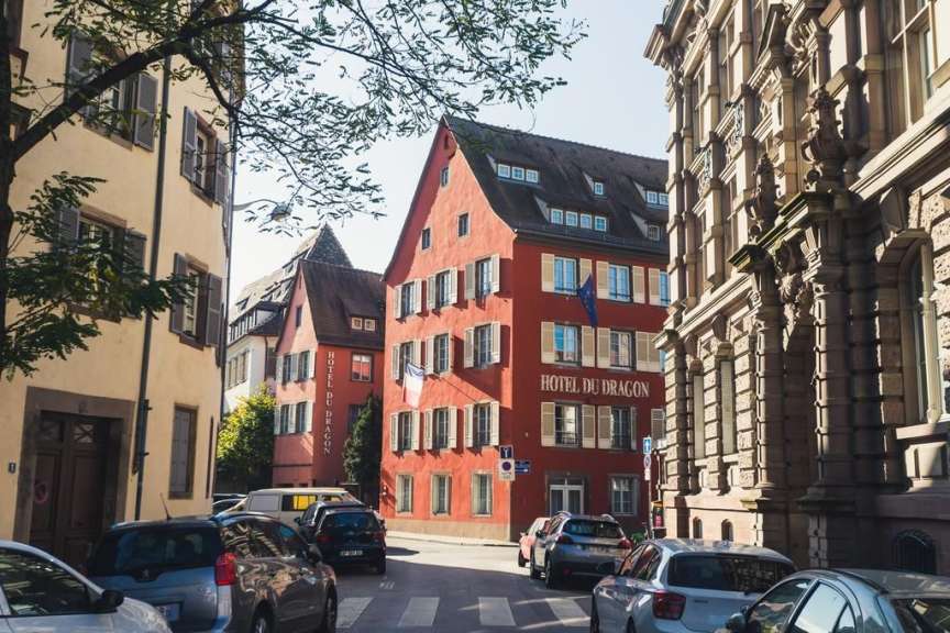 Die Aufnahme zeigt eine schmale Straße mit Häusern, Autos und Bäumen.