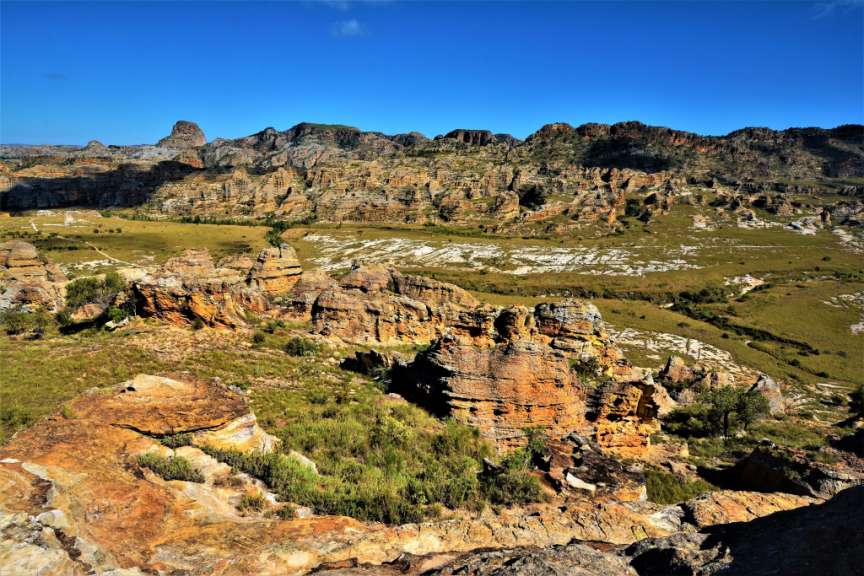 Ein weites Landschaftspanorama in Madagascar mit zerklüfteten Felsformationen und grünen Tälern unter einem strahlend blauen Himmel.