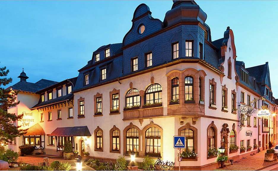 Das Bild zeigt ein Hotel mit traditioneller Architektur am Abend, beleuchtet von innenliegendem Licht.