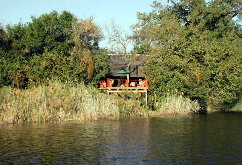 Ein Hausboot mit einem Dach aus Stroh liegt in einem Fluss, umgeben von üppiger Vegetation.