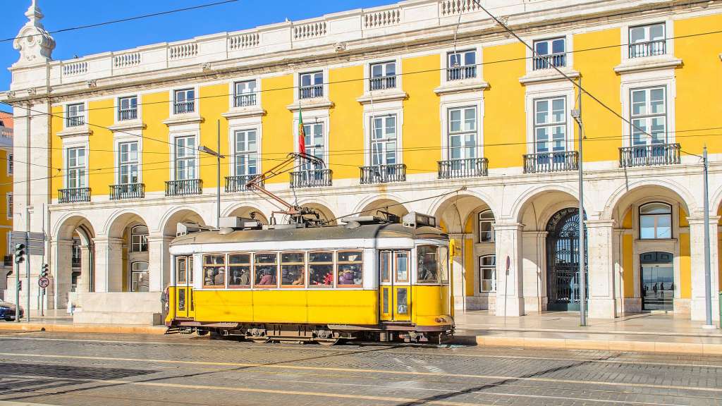 Eine gelbe Straßenbahn fährt vor einem großen gelben Gebäude