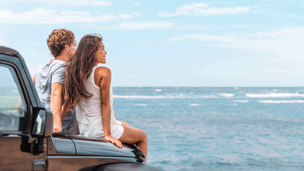 Ein Paar sitzt auf der Motorhaube eines Autos und blickt auf das Meer.