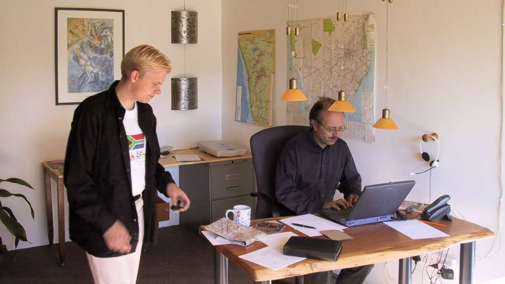 Ein Mann steht neben einem Mann, der an einem Schreibtisch sitzt und einen Laptop benutzt
