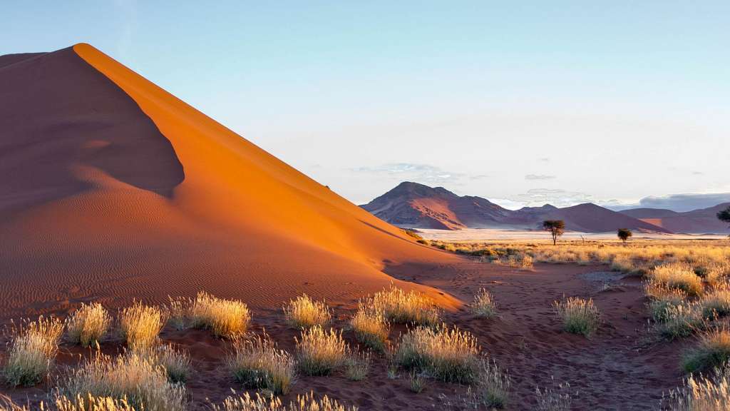 Eine große Sanddüne in der Wüste mit Bergen im Hintergrund