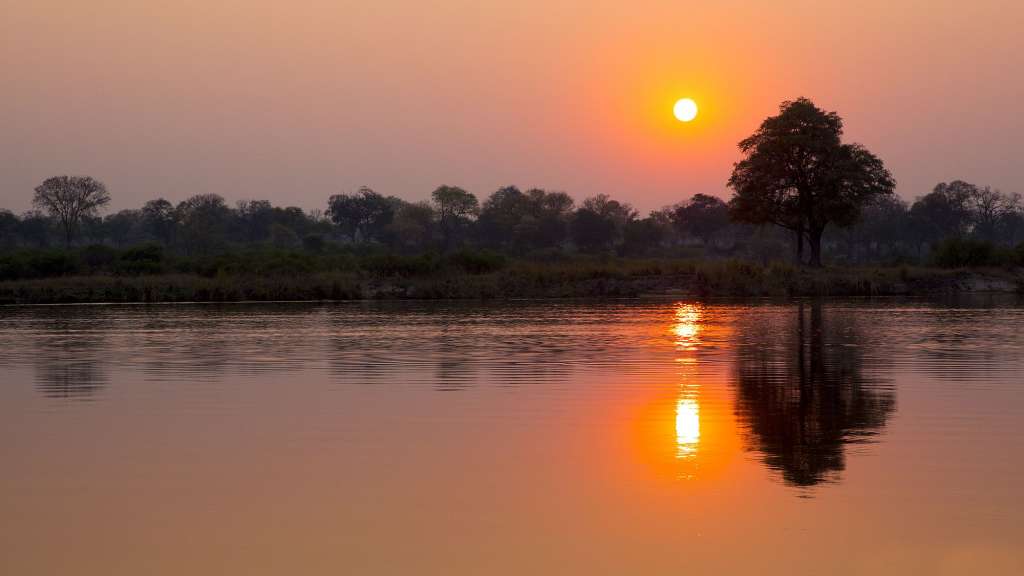 Die Sonne geht über einem Fluss mit Bäumen im Hintergrund unter