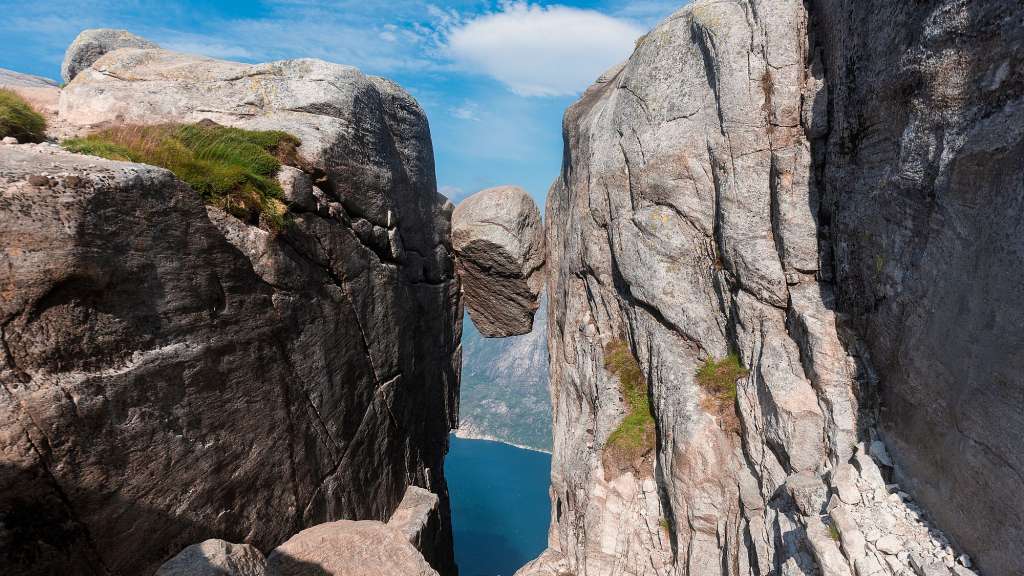 Ein Felsvorsprung hängt zwischen zwei steilen Felsen über einer tiefblauen Bucht.