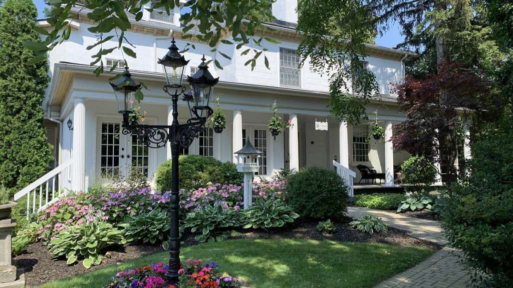Ein großes weißes Haus mit einer Veranda und einem Blumenbeet