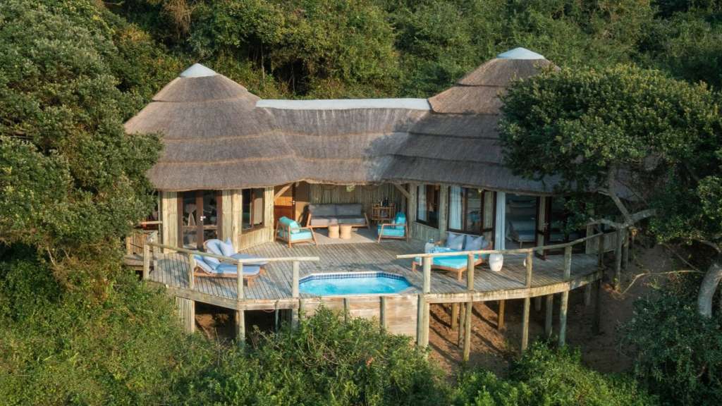 Ein Haus mit Strohdach und einem Pool auf einem Holzdeck