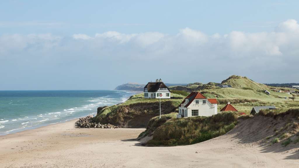 Ein weißes Haus mit einem roten Dach sitzt auf einem Hügel über einem Strand