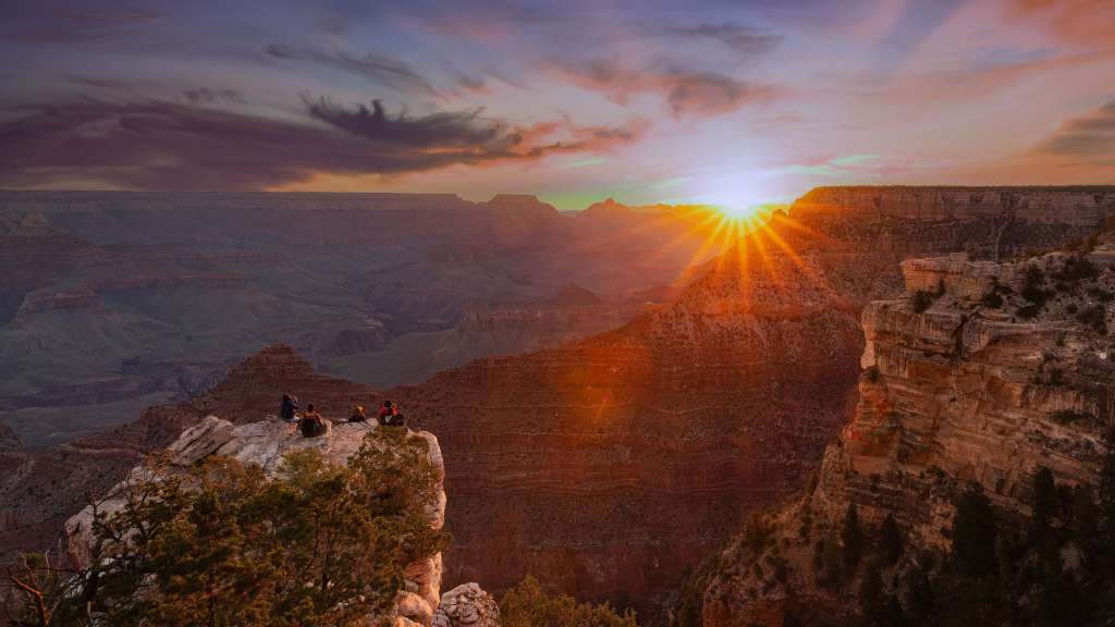 Eine Gruppe von Menschen sitzt auf einer Klippe mit Blick auf den Sonnenuntergang