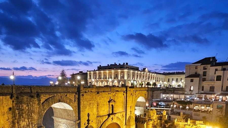 Diese Aufnahme zeigt eine romantische Abendstimmung über einer alten Brücke mit beleuchteten Gebäuden im Hintergrund.