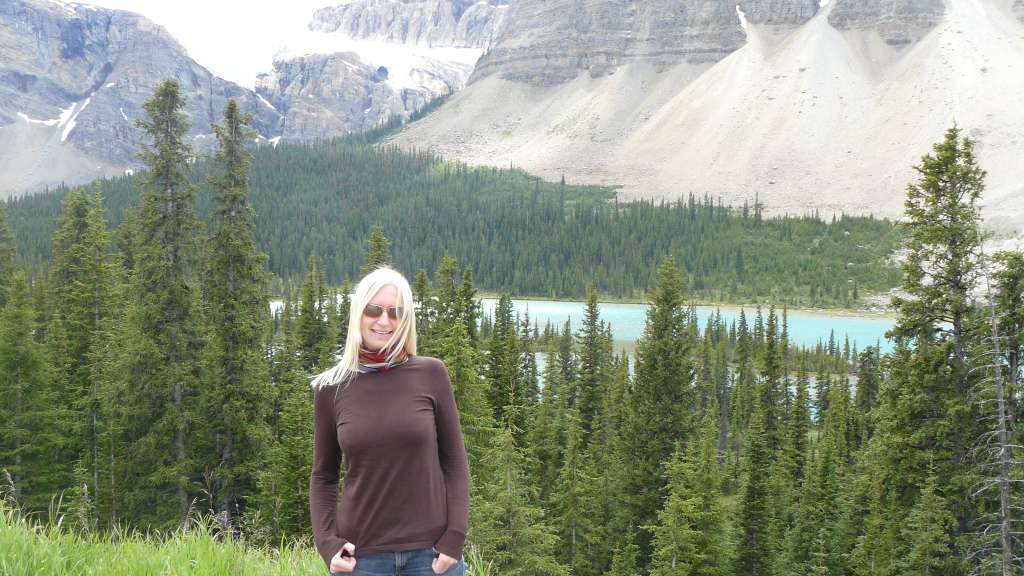 Eine Frau steht in der Natur vor einem See und einem Berg.