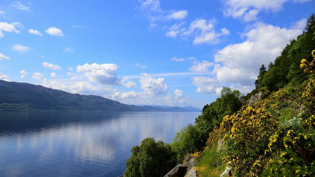 Ein See mit Bergen im Hintergrund und einem blauen Himmel mit Wolken