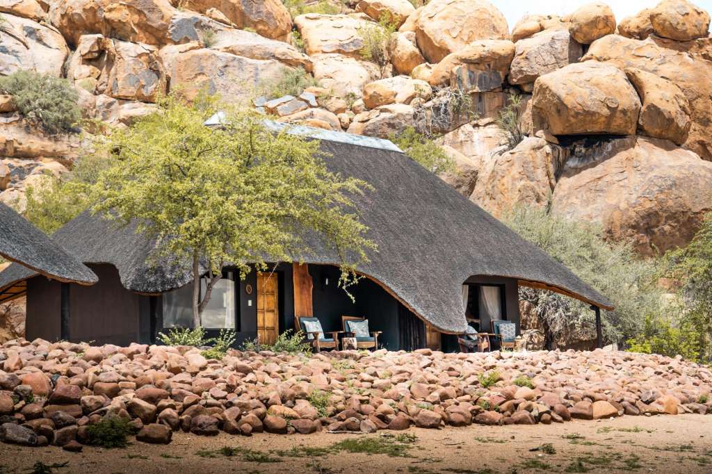 Ein schwarzes Haus mit Strohdach steht inmitten einer felsigen Landschaft