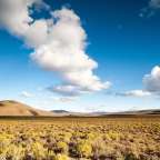 Ein Feld mit Bergen im Hintergrund und einem blauen Himmel mit Wolken