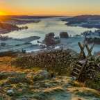 Die Sonne geht über einen See mit einer Steinmauer im Vordergrund